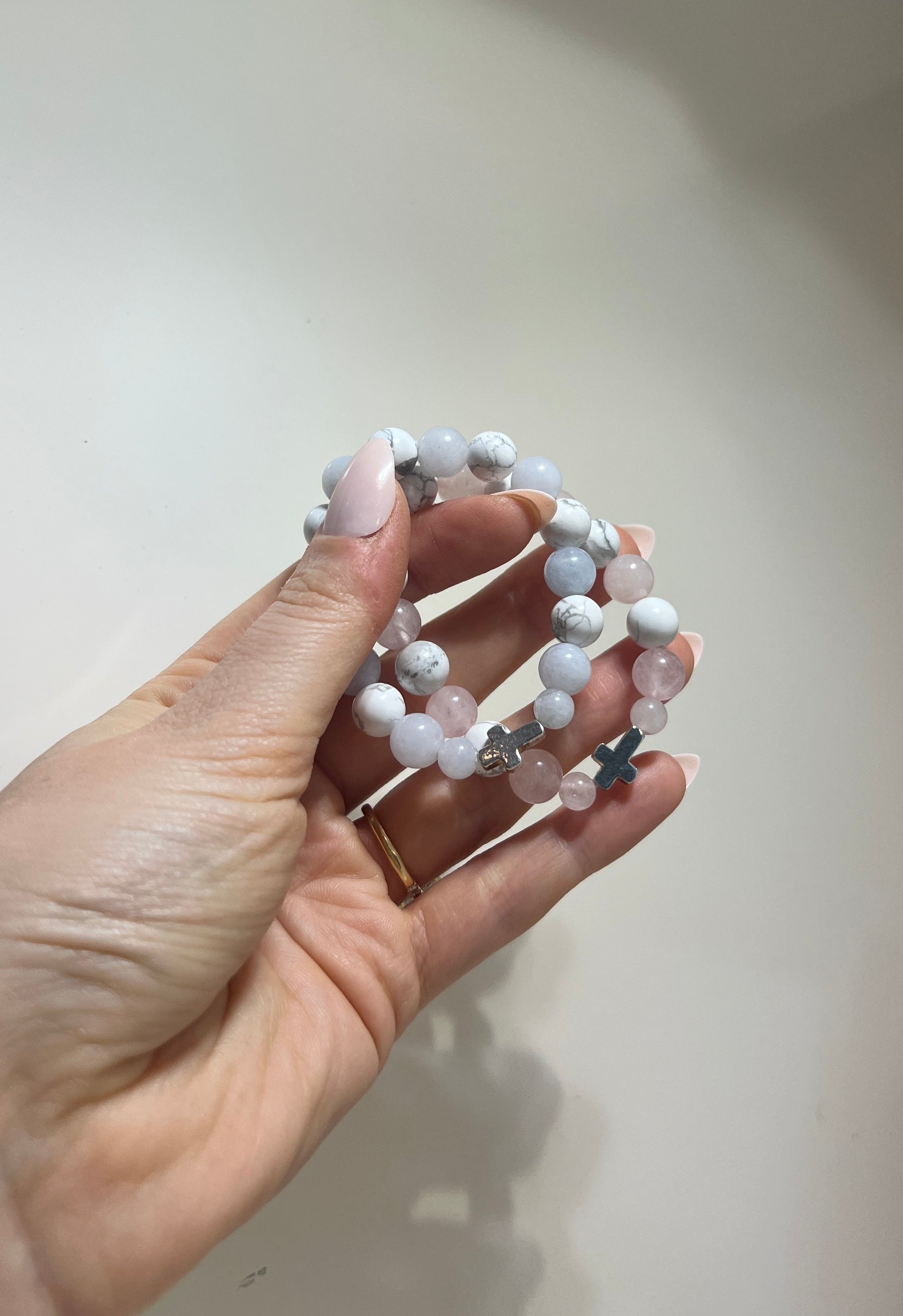 Hand holding a bracelet with white beads against a plain background