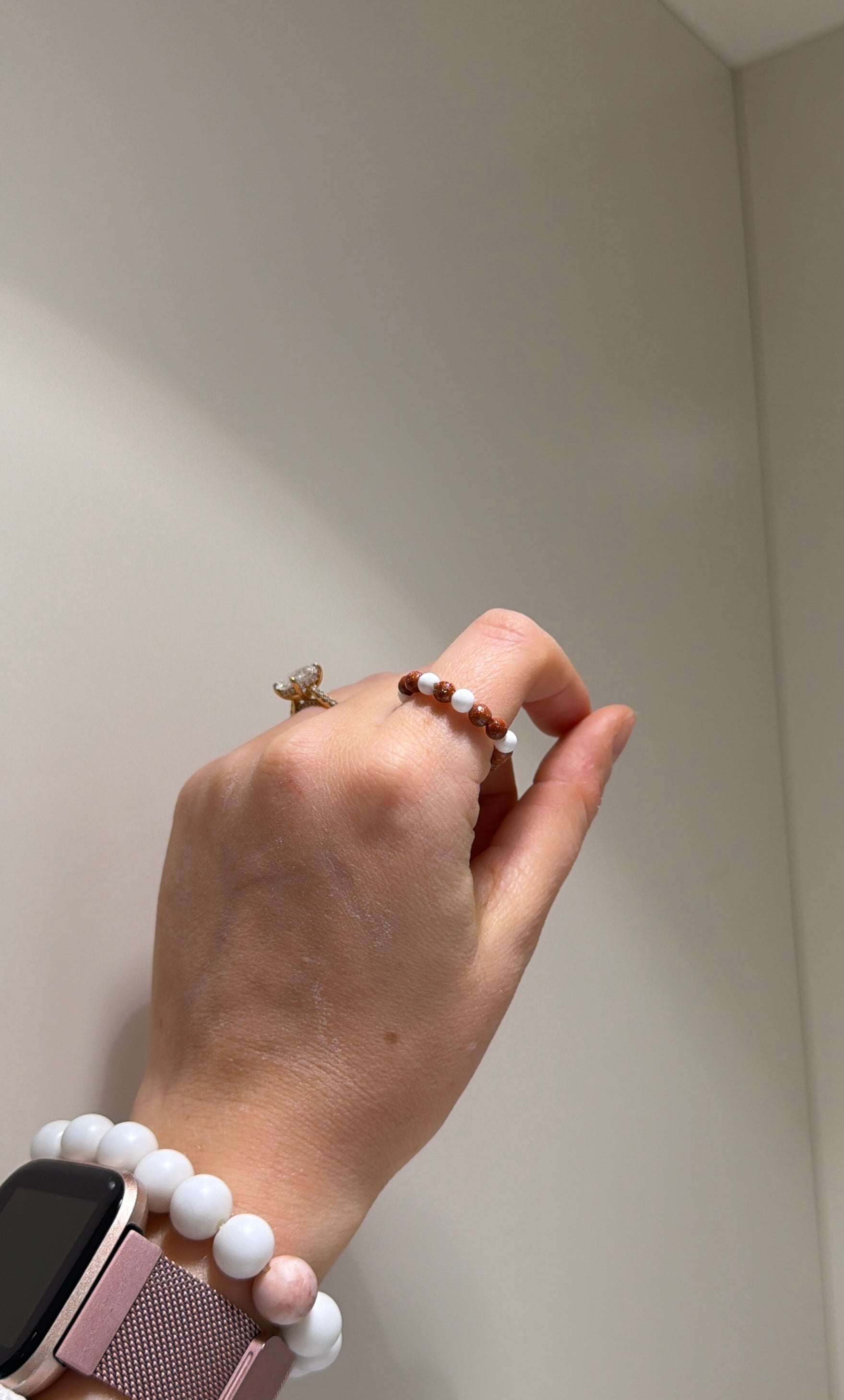 Hand wearing a bracelet and ring against a neutral background