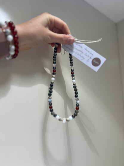 Beaded necklace held by a hand with a visible tag against a neutral background