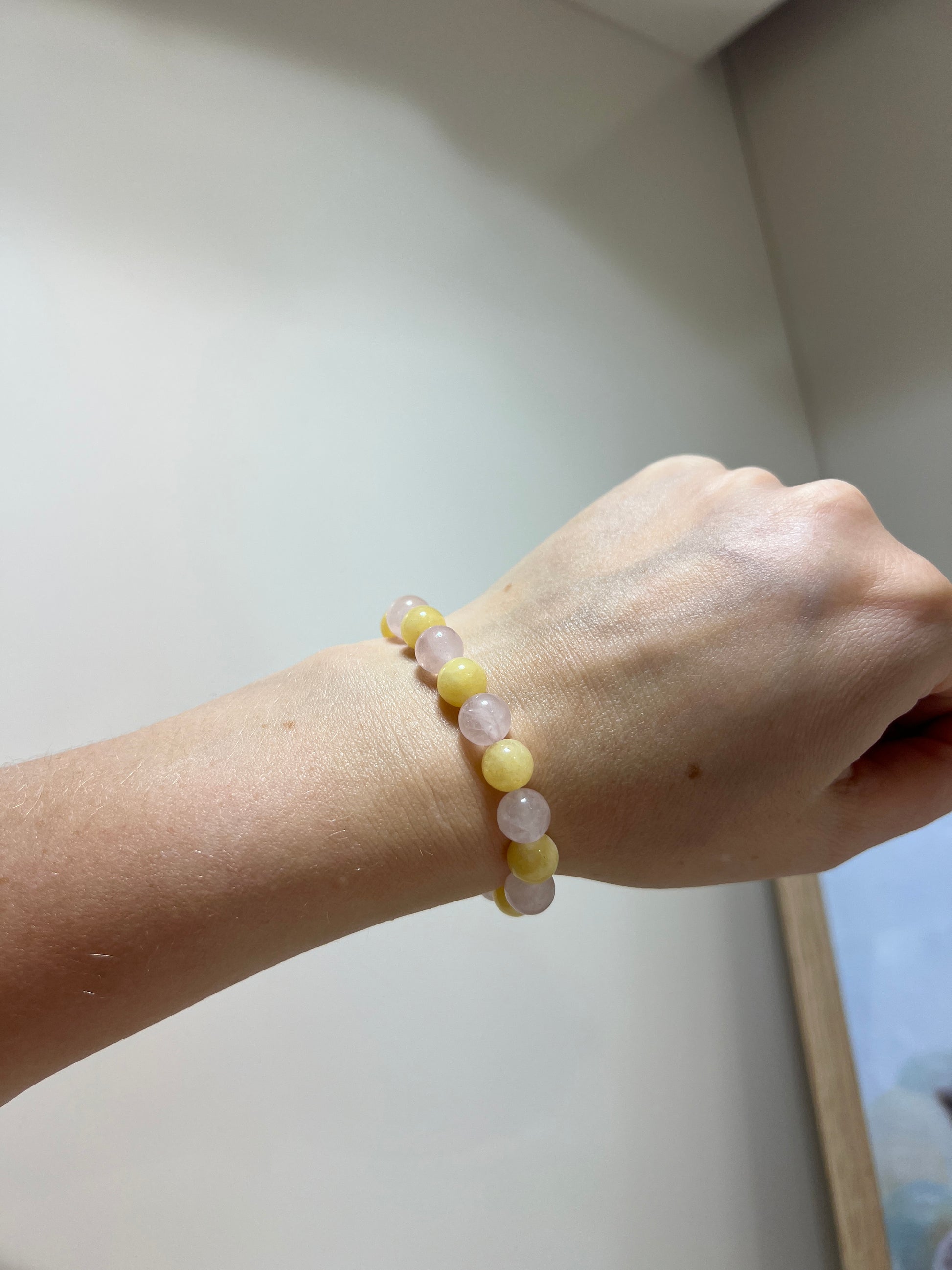 Hand wearing a bracelet with yellow beads on a light background