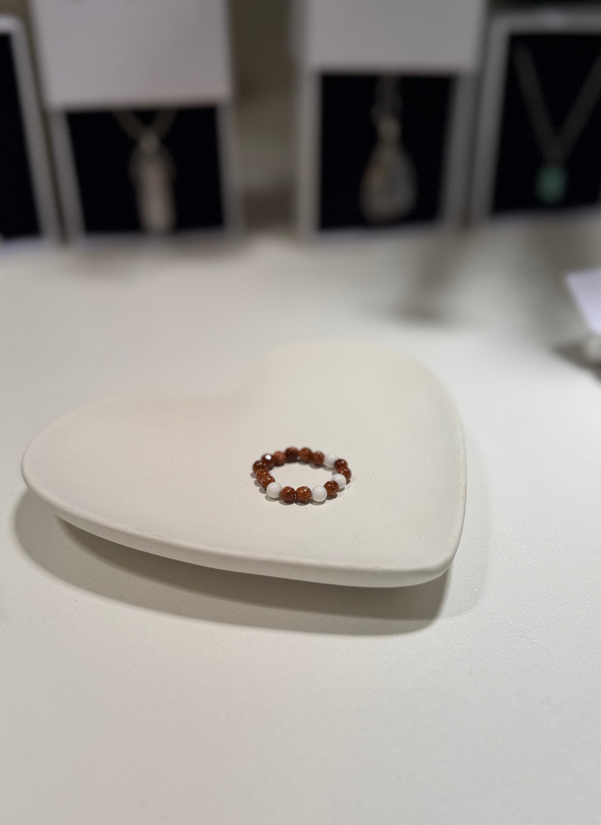 Beaded ring in a heart-shaped box on a white surface with blurred background