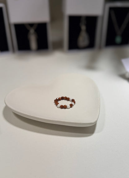 Beaded ring in a heart-shaped box on a white surface with blurred background