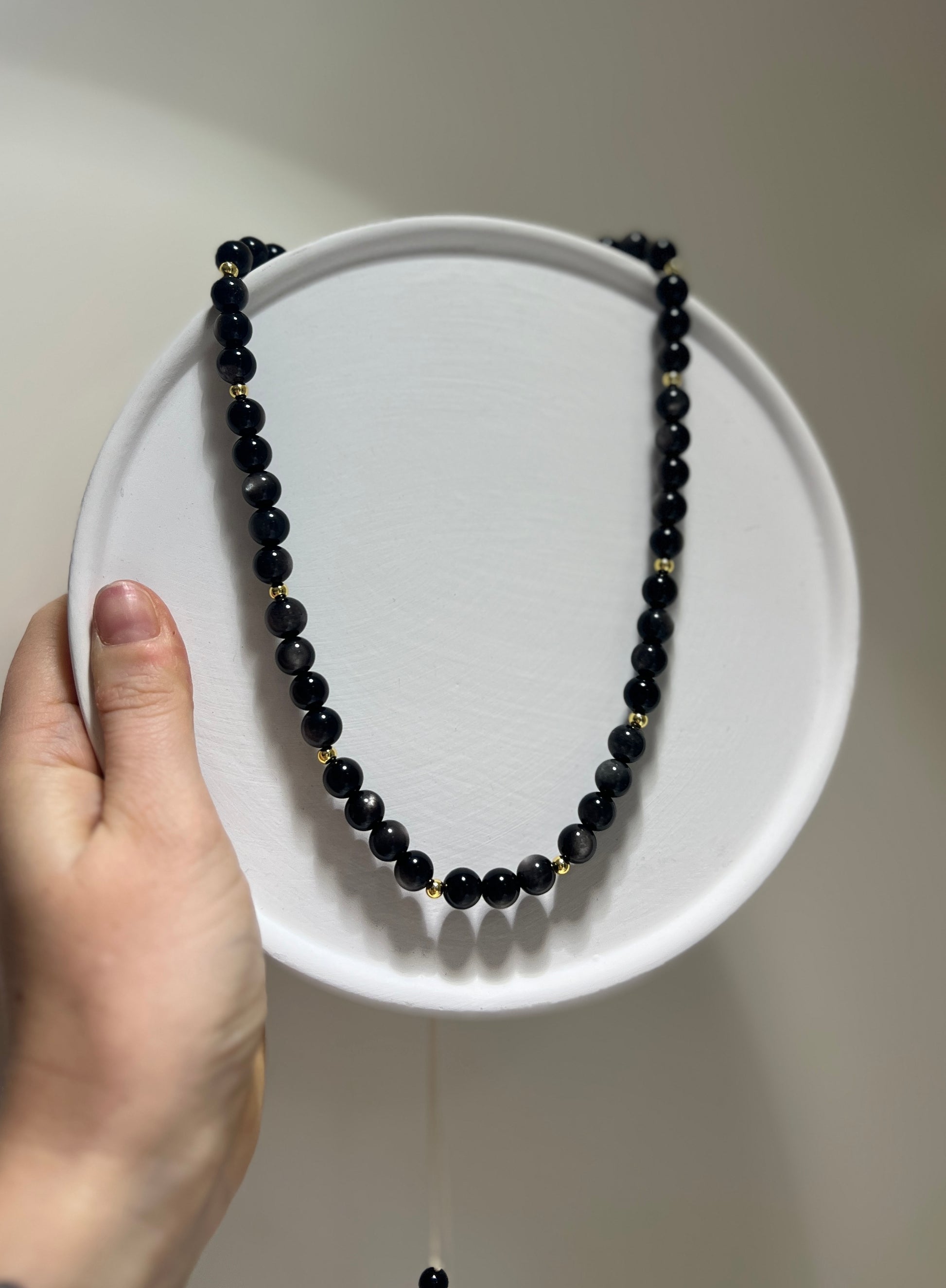 Black beaded necklace on a white plate held by a hand against a neutral background