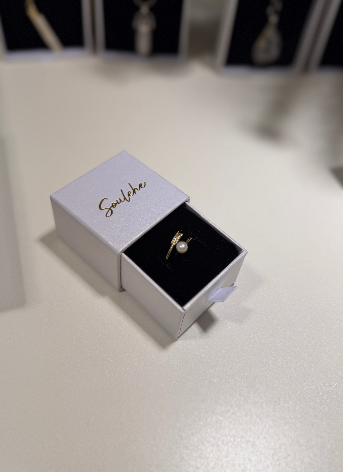 Gold ring in an open jewelry box with 'Soulehe' branding on a light surface.