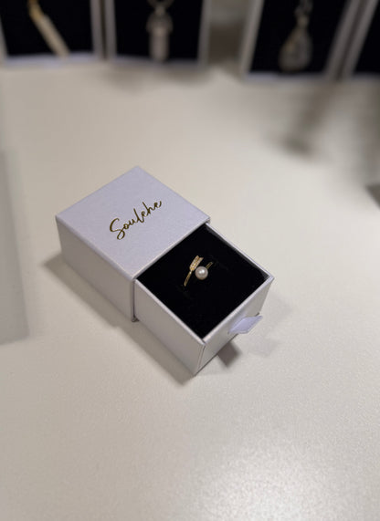 Gold ring in an open jewelry box with 'Soulehe' branding on a light surface.