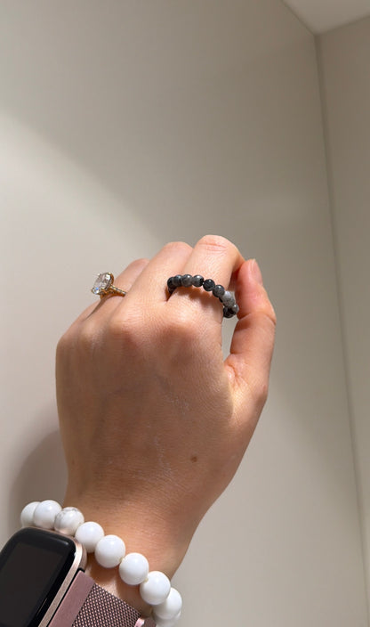Hand wearing a ring and bracelet against a neutral background