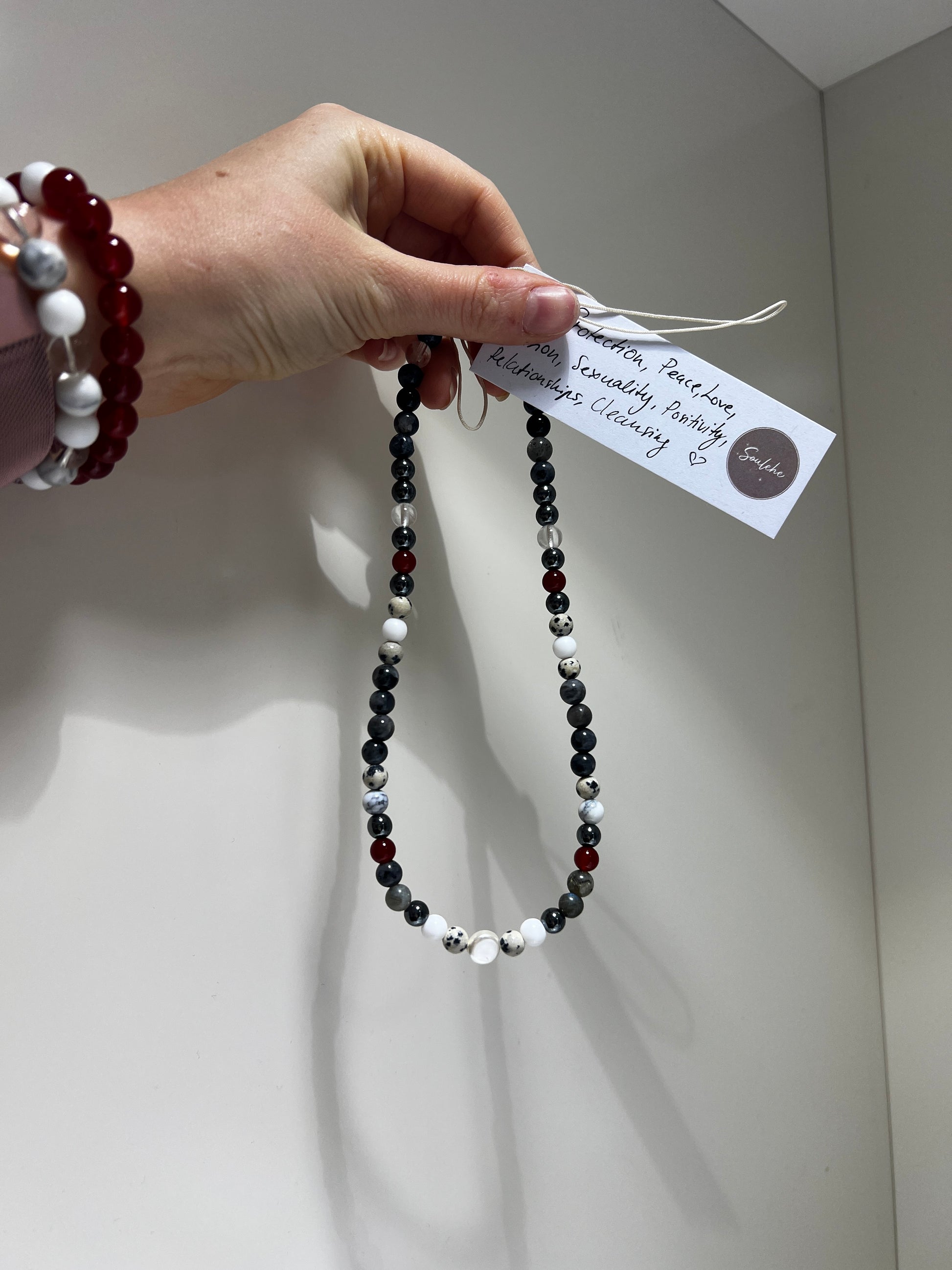 Beaded necklace held by a hand with a white card, against a neutral background