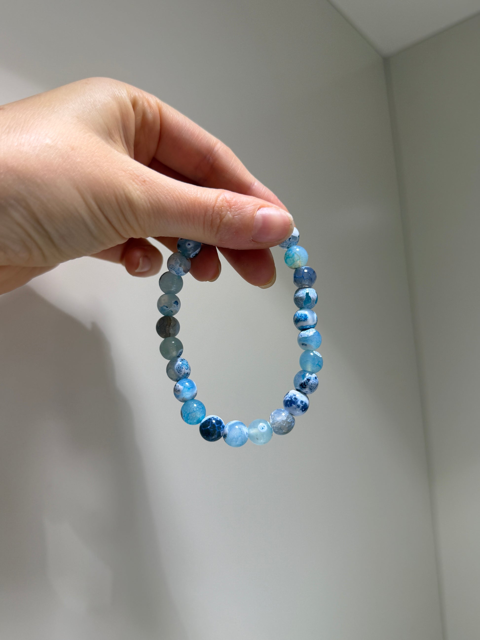 Hand holding a blue beaded bracelet against a plain background