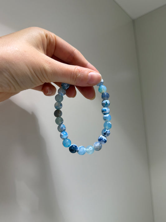 Hand holding a blue beaded bracelet against a plain background