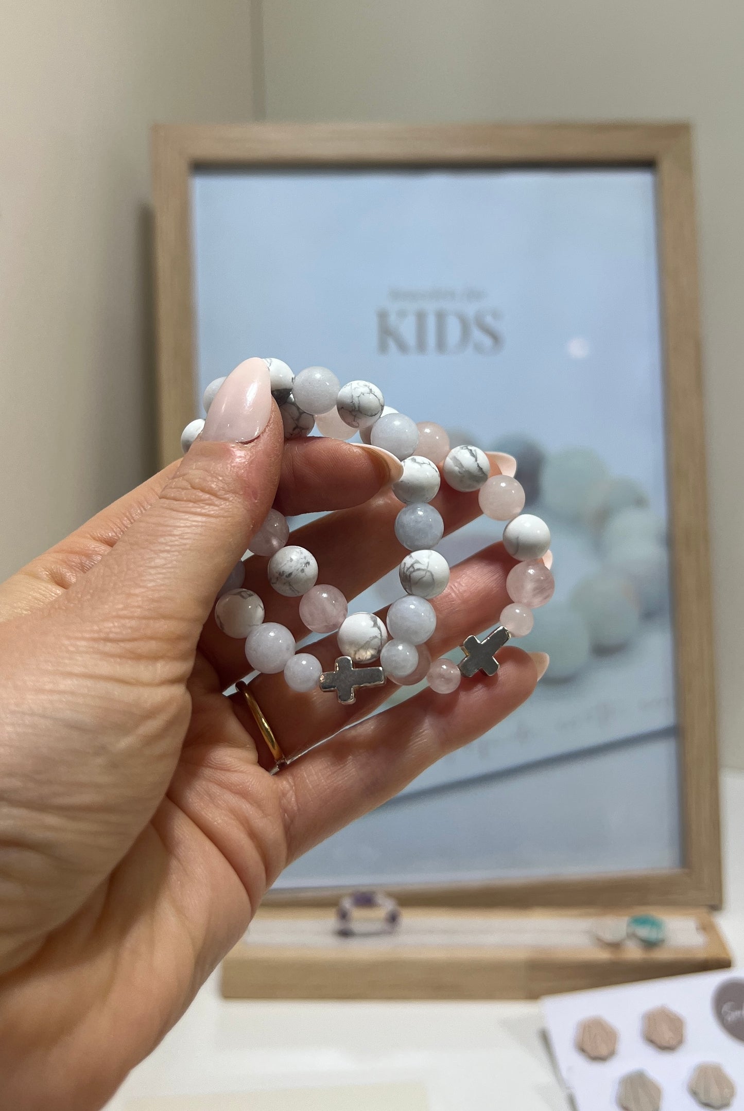 Hand holding a stack of white beaded bracelets with a 'KIDS' sign in the background