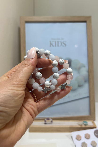 Hand holding a stack of white beaded bracelets with a 'KIDS' sign in the background