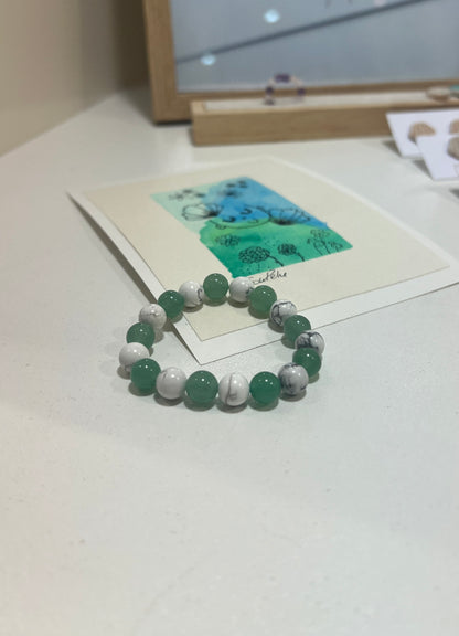 Green and white beaded bracelet on a white surface with a blurred background